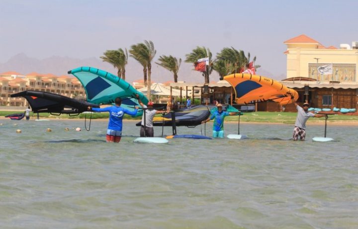 Wing foil lesson in a shallow lagoon, riders standing in the water holding their wings beside their foil boards