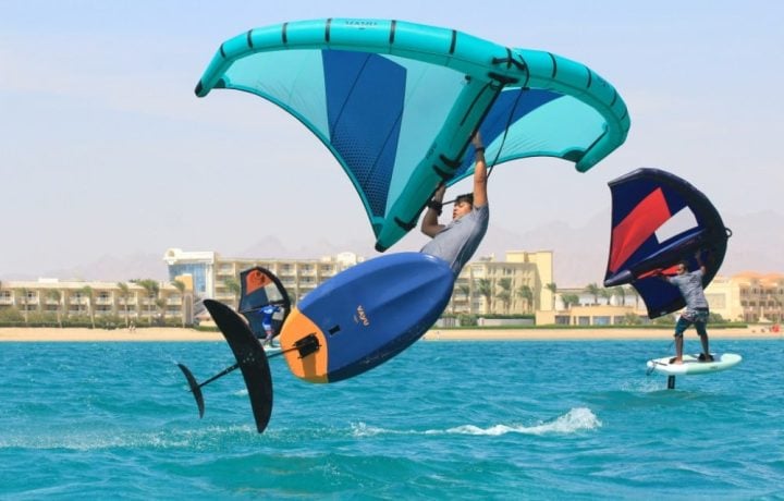 Wing foiler lifting off with the hydrofoil visible under the board, and a second rider foiling behind