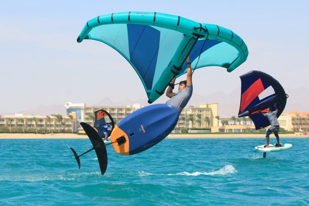 Wing foiler lifting off with the hydrofoil visible under the board, and a second rider foiling behind